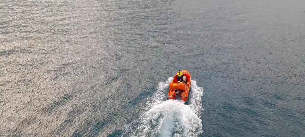 A small orange tender boat driving in the sea.